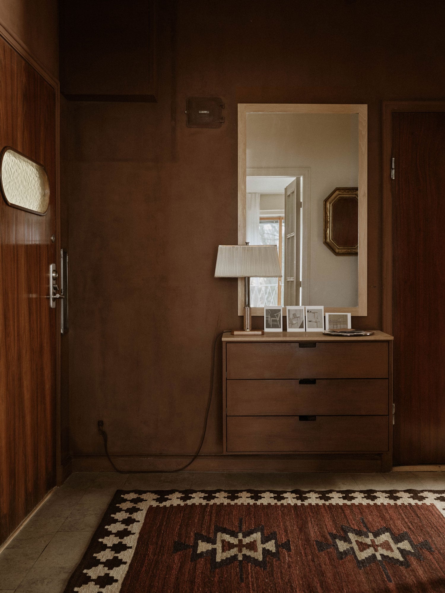 chest of drawers and mirror in a hallway with brown walls and the logo ‘Enter gently and leave the outside behind’